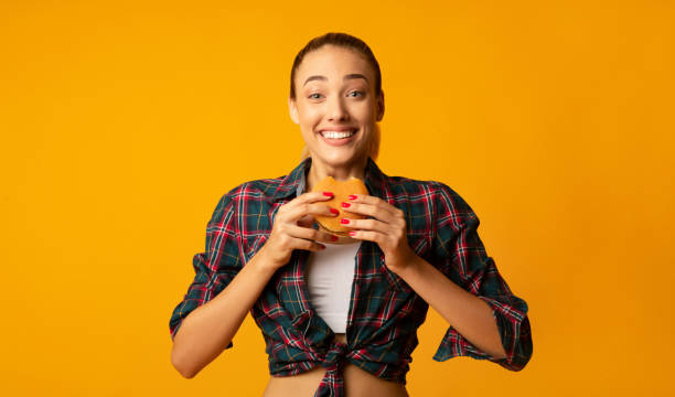 istock Slim Girl Eating Burger Over Yellow Studio Background 1169128469