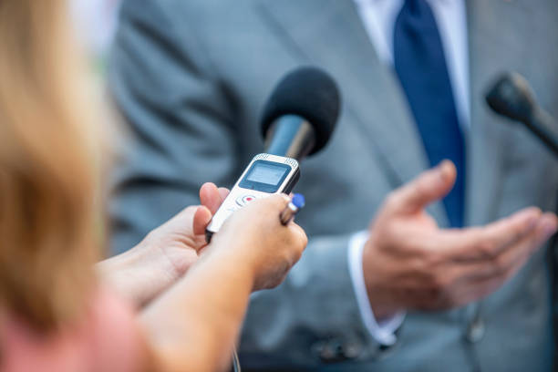 An unrecognizable public speaker or professor sits on a stage and speaks publicly through a microphone at a meeting or public lecture, copy space