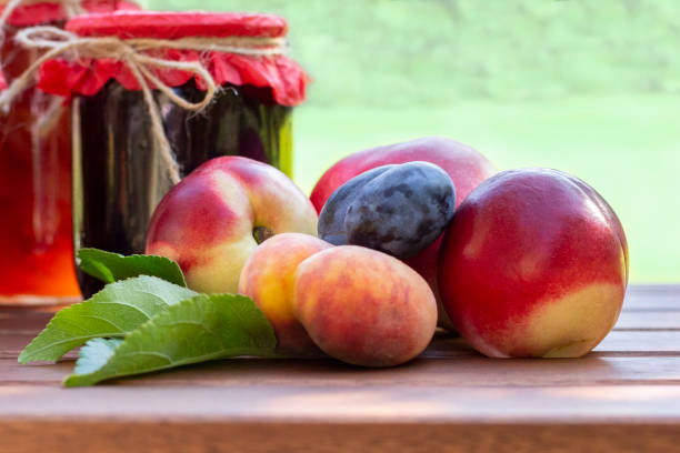 fresh fruits and homemade jars of jam on wooden table in blurred natural  garden background. preserves of peaches, nectarines, plums. - preserves jar apricot marmalade imagens e fotografias de stock