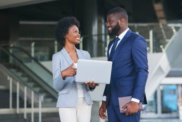 Young woman pointing finger to laptop screen while standing outdoors Young african woman pointing finger to laptop screen while standing outdoors with her colleague african american business couple stock pictures, royalty-free photos & images