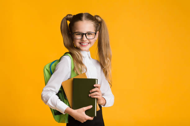 istock Smiling Elementary School Girl Holding Books Posing Over Yellow Background 1169134549