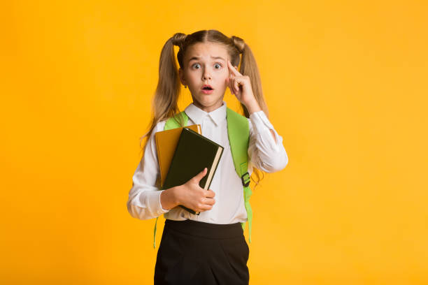 istock Embarassed Elementary Student Looking At Camera Holding Books On Yellow Background 1169134562