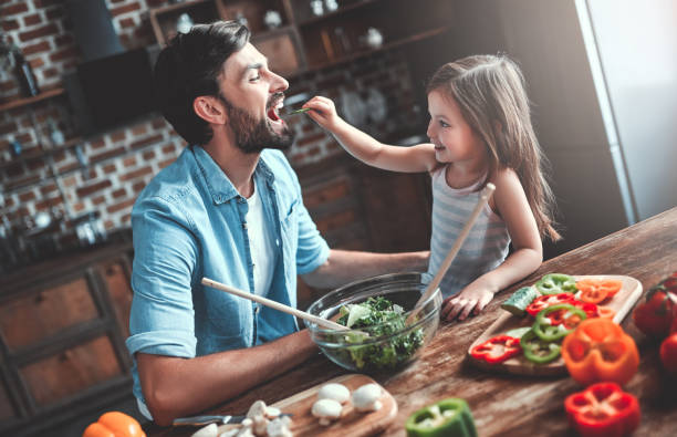 Dad with daughter on kitchen Handsome man and his little cute daughter are cooking on kitchen. Making salad. Healthy lifestyle concept. family dinners and cooking stock pictures, royalty-free photos & images