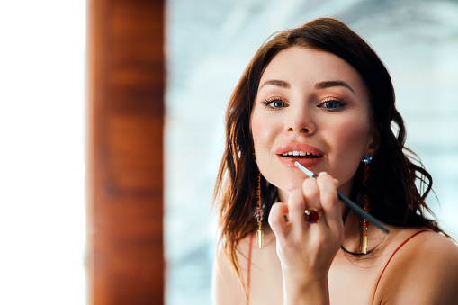 Shot of a glamorous young woman applying lipstick with a brush in front of a mirror