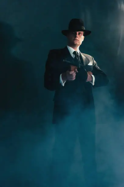 Photo of Retro gangster in hat in misty night shoots with machine gun.