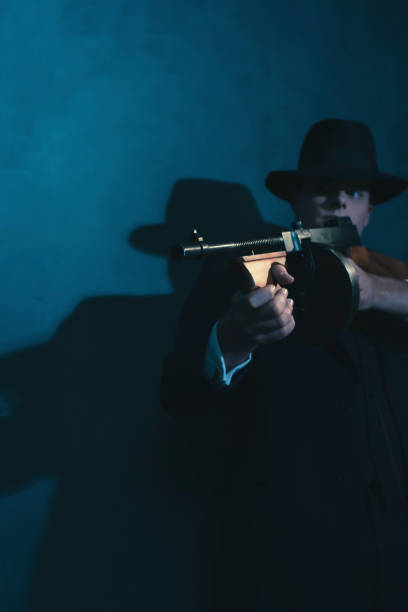 istock Retro gangster in hat shoots with machine gun. 1169137479