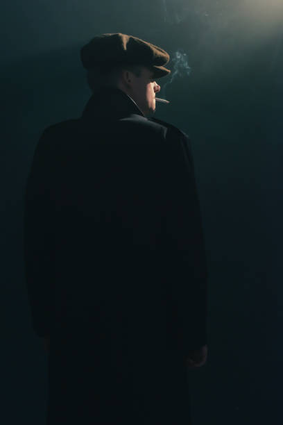 istock Retro man with cap smokes cigarette in smoky room. Side view. 1169137582