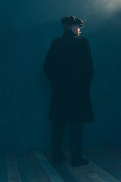 istock Retro man with cap smokes cigarette in smoky room. Side view. 1169137588
