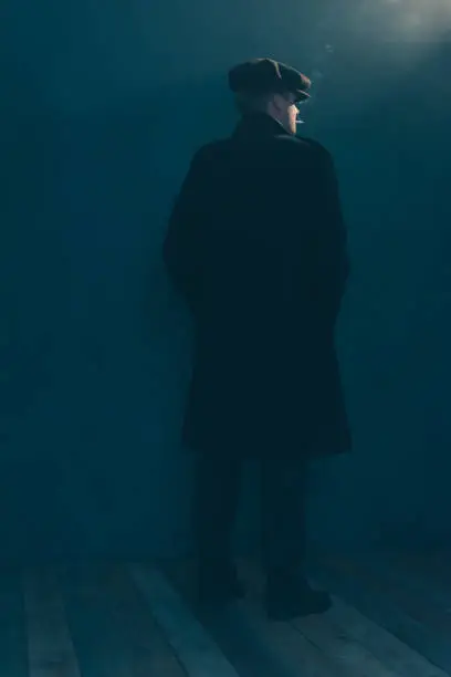 Photo of Retro man with cap smokes cigarette in smoky room. Side view.