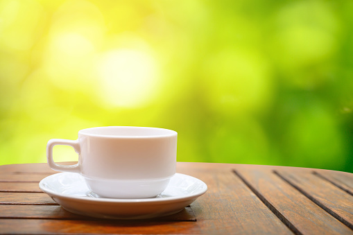 A white coffee mug placed on a wooden table in a natural garden