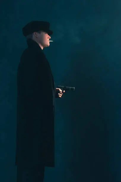 Photo of Retro mobster with cigarette shoots with gun. Side view.