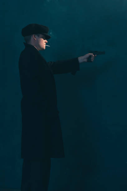 istock Retro mobster with cigarette shoots with gun. Side view. 1169137838