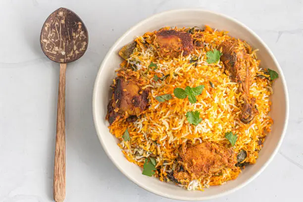 Chicken Dum Biryani in a Bowl and a Serving Spoon on White Background Directly Above Photo.
