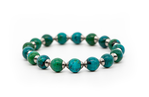 Bracelet made of blue and green chrysocolla stone on a white background, close-up, selective focus.