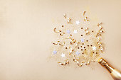 Champagnerflasche mit Konfetti-Sternen, Glitzer und Party-Streamer auf goldenem Hintergrund. Weihnachten, Geburtstag oder Hochzeit Konzept. Flat-Lay-Konzept.