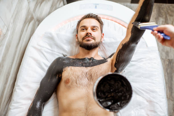 Man during a mud wrapping Man during a mud wrapping with special black mud, lying in the spa salon. Concept of a Detox mud body wraps people covered in mud stock pictures, royalty-free photos & images