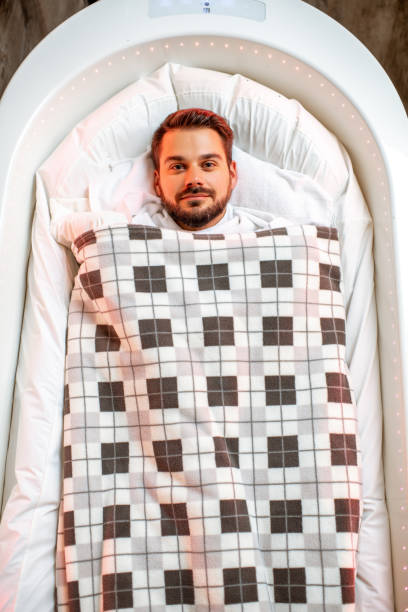 Wrapped man lying in the spa capsule Man lying in the hot SPA capsule wrapped with bedcover during the mud wrap procedure in the SPA salon people covered in mud stock pictures, royalty-free photos & images