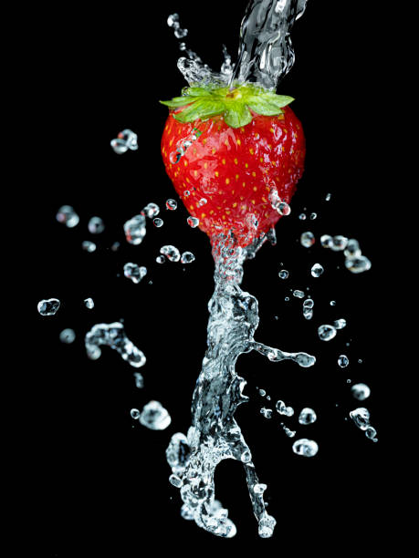 Fresh strawberries are just thrown into water. They make bubbles while going deep into the crystal clear water on white background.