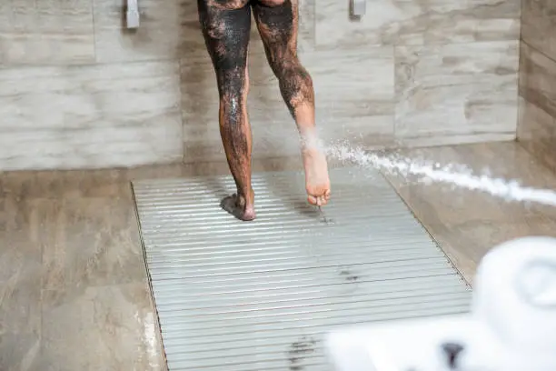 Man having high pressure shower on his feet after the mud wrapping procedure at the luxury SPA salon. Concept of hydrotherapy and Sharko shower