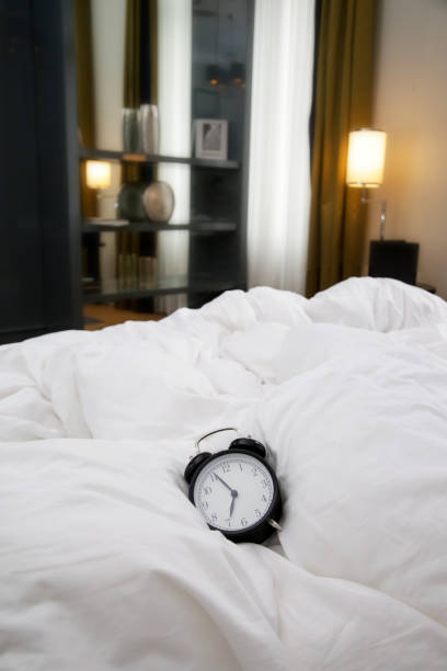 istock Classic black alarm clock on the white wrinkled bed sheets 1169155153