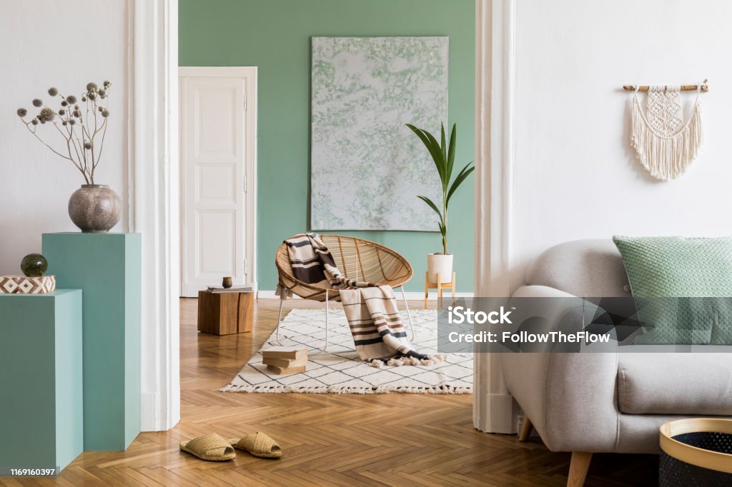 Modern and bohemian composition of interior design at apartment with gray sofa, rattan armchair, wooden cubes, plaid, tropical plant, macrame and elegant accessories. Stylish home decor. Template. Interior design of living room at modern home with stylish furnitures. Design home decor. Template. Living Room Stock Photo