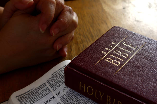 istock Holy Bible on a table and hands in praying position 1169161031