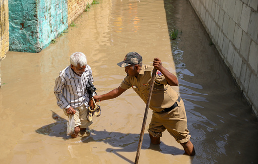 A Police officer helps an old man as they walk in flood water in a residential area near the banks of the overflowing Yamuna River in New Delhi, India.