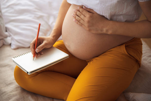 istock Pregnant young lady writing in spiral notebook 1169163677