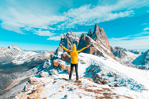 Man celebrating success at top of snowy mountain. Hiker wearing a yellow jacket and looking at a beautiful view. Outdoors and sport concepts in Italian Alps mountains.