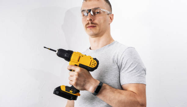 Construction: A man in protective glasses is holding a yellow electric screwdriver. Construction: A man in protective glasses is holding a yellow electric screwdriver. Close-up. holding drill stock pictures, royalty-free photos & images