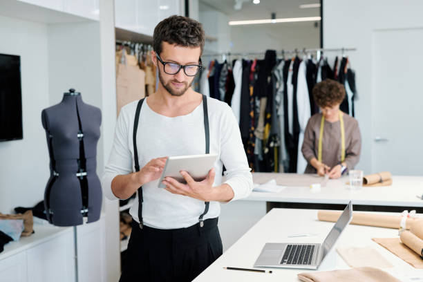 istock Young serious male tailor with tablet looking through online creative ideas 1169167531