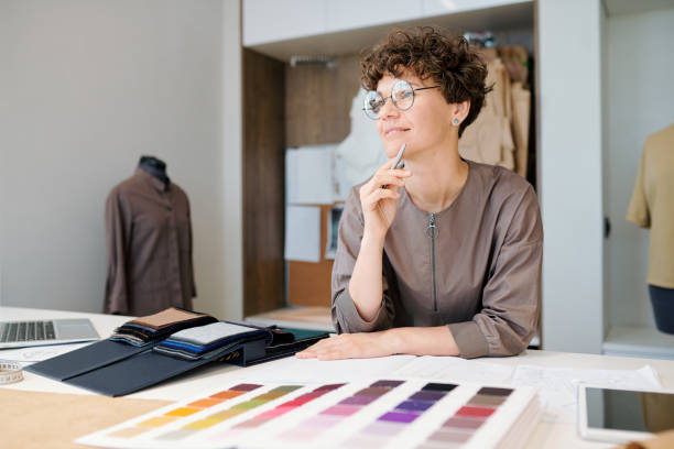 istock Happy young female creative designer thinking of ideas by workplace 1169167675