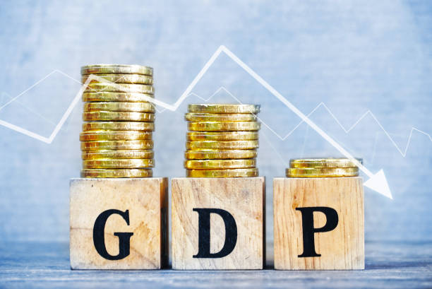 istock GDP text on wood cube and gold coins stack volume with trend direction down side , finance and economic concept. 1169169887