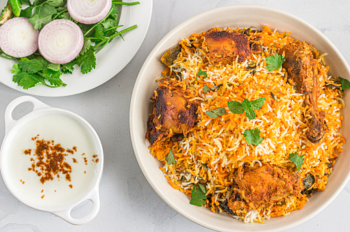 Chicken Dum Biryani in a Pot with Raita and Onion on White Background Top View Photo.