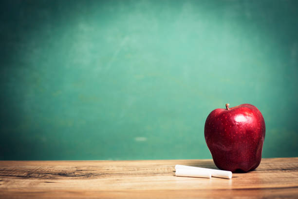 istock Apple, chalk on wooden school desk with chalkboard. 1169173322