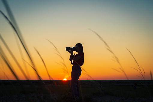 Photographer girl photographing sunset with dslr