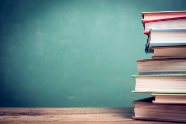 Back to school. Textbooks stacked on wooden school desk in front of green chalkboard. Classroom setting.