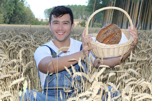 Ethnic farmer holding bread in wheat field.