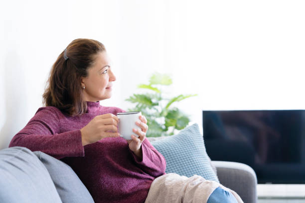 istock Middle aged lady sitting on sofa holding coffee or tea mug 1169176039