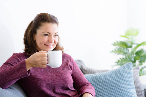 istock Middle aged lady sitting on sofa holding coffee or tea mug 1169176065