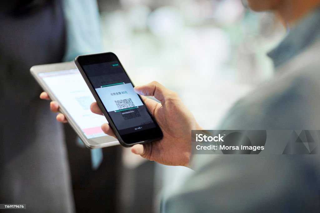 Man paying through smart phone in cafe Midsection of man paying waitress through smart phone. Barista receiving contactless payment from customer. They are in cafe. Paying Stock Photo