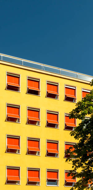 facciata di un hotel o di un edificio per uffici degli anni '60, intonaco con vernice gialla e prendidi esteso in rosso vivo con un motivo interrotto sotto il sole splendente e cieli blu - sunblinds foto e immagini stock