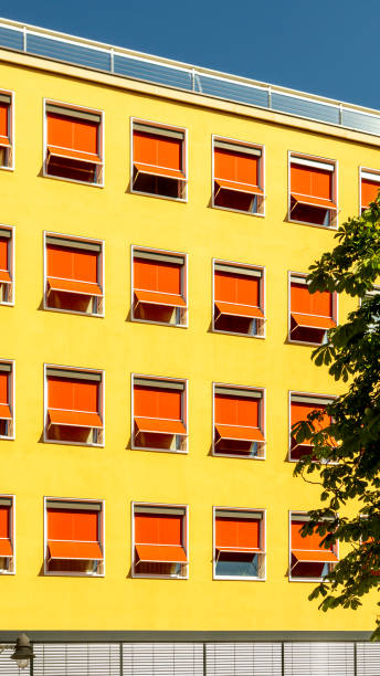 facade of a hotel or office building from the 60s, plaster with yellow paint and sunblinds extended in bright red with an interrupted pattern in bright sunshine and blue skies - sunblinds imagens e fotografias de stock