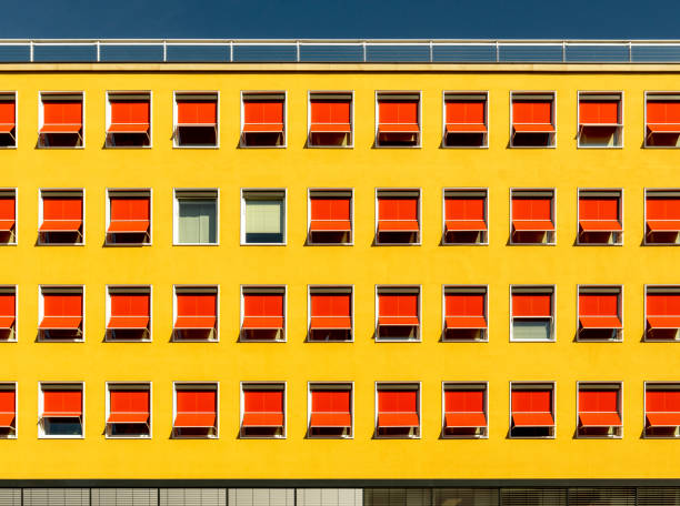 facciata di un hotel o di un edificio per uffici degli anni '60, intonaco con vernice gialla e prendidi esteso in rosso vivo con un motivo interrotto sotto il sole splendente e cieli blu - sunblinds foto e immagini stock