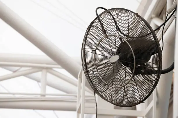 Photo of black mist fan hang on steel structure under roof. spinning big industrial fan.