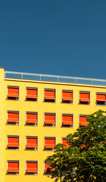 facciata di un hotel o di un edificio per uffici degli anni '60, intonaco con vernice gialla e prendidi esteso in rosso vivo con un motivo interrotto sotto il sole splendente e cieli blu - sunblinds foto e immagini stock