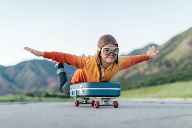 Young Boy Ready to Travel with Suitcase A young boy wearing flying goggles and flight cap has packed his suitcase and has placed it on a skateboard. He is ready to fly away with arms outstretched to the destination of his dreams. Image taken in Utah, USA. arms outstretched photos stock pictures, royalty-free photos & images