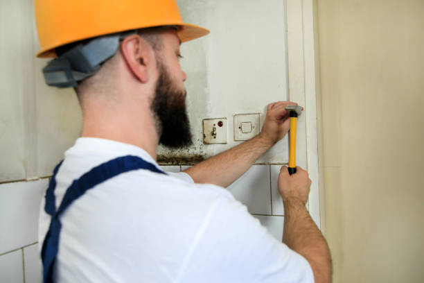 istock Construction worker and handyman working on renovation work. Builder with yellow hammer strikes and nails a nail into wooden wall of kitchen door at construction site. Apartment renovation concept. 1169206179