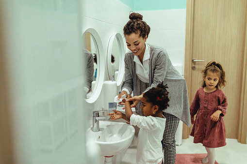 Teacher and little girls washing hands in the bathroom at kindergartner