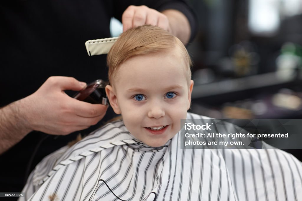 Cute Blond Smiling Baby Boy With Blue Eyes In A Barber Shop Having Haircut  By Hairdresser Hands Of Stylist With Tools Children Fashion Stock Photo -  Download Image Now - iStock